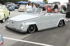 an old car parked in a parking lot next to other antique cars and people standing around