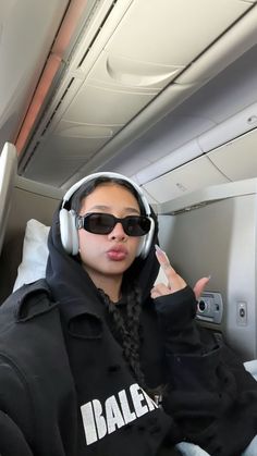 a woman wearing headphones on an airplane with her hand up in the air and pointing