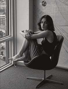 a black and white photo of a woman sitting in an office chair looking out the window