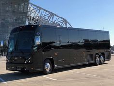 a large black bus parked in a parking lot next to a tall building with a metal roof