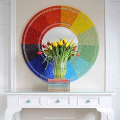 a white table topped with a vase filled with flowers next to a rainbow painted wall