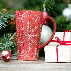 a red coffee mug with white snowflakes on it next to presents and christmas trees