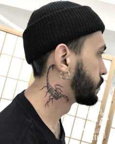 a man with a scorpion tattoo on his neck and behind his ear, wearing a beanie