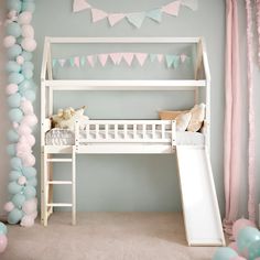 a white bunk bed sitting next to a slide in a room filled with pink and blue balloons