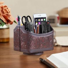 a cell phone holder with pens, pencils and other office supplies in it on a desk