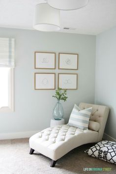 a white chaise lounge chair sitting in front of four framed pictures on the wall