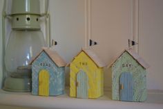 three small wooden houses sitting on top of a white shelf next to a glass jar