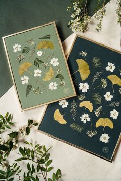 two cards with gold leaf designs on them next to some white flowers and greenery