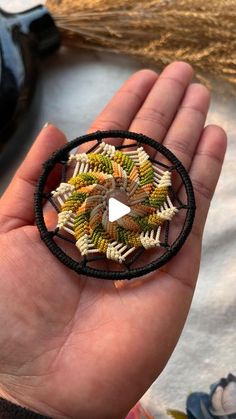 a hand holding a small beaded brooch in it's palm, with a video playing on the screen