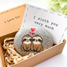 two sloths sitting on top of each other in a box next to a note