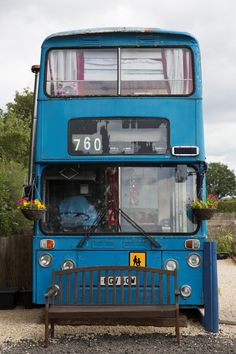 a blue double decker bus parked next to a wooden bench