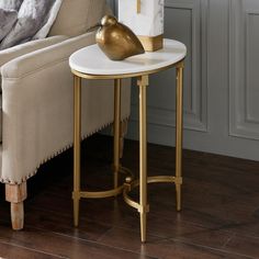 a white and gold end table with a clock on it next to a couch in a living room