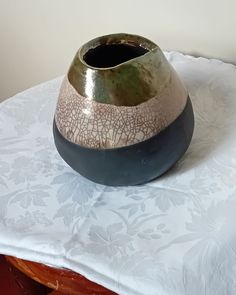 a ceramic vase sitting on top of a white tablecloth covered table with a flowered design