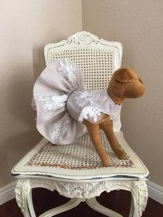 a stuffed dog in a white dress sitting on a chair