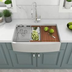 a kitchen sink filled with green apples and grapes next to a cutting board on top of a counter