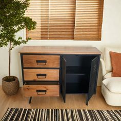 a room with a white chair and a wooden cabinet next to a tree in the corner