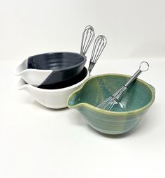 two bowls with whisks in them on a white surface