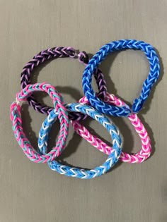 four different colored braided bracelets sitting on top of a gray surface with one knot in the middle