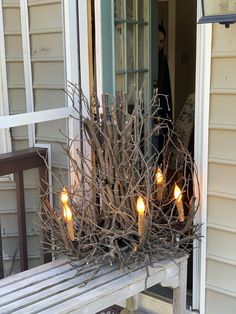 candles are lit on the branches of a tree in front of a door way with a man standing behind it