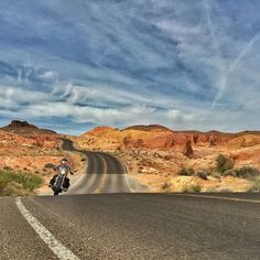 a man riding a motorcycle down the middle of a desert road