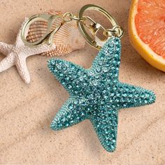 a starfish keychain and an orange slice are on the sand next to each other