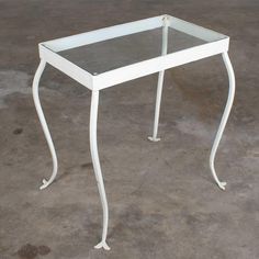 a glass table sitting on top of a cement floor next to a white metal frame