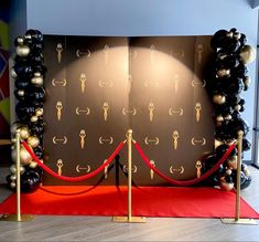 a red carpet with black and gold balloons on it next to a wall that has an arch