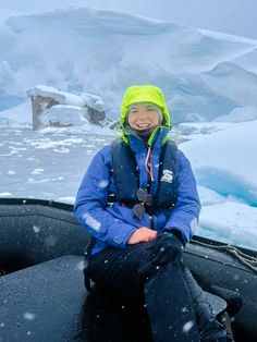 a person sitting on the back of a boat in the snow with an iceberg behind them