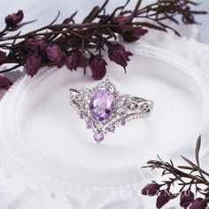 a purple ring sitting on top of a white plate next to some flowers and leaves