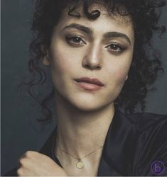 a woman with curly hair wearing a black shirt and gold necklace, posing for the camera