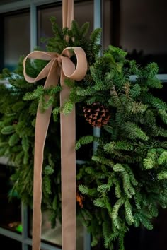 a christmas wreath with a bow and pine cones hanging from it's front door