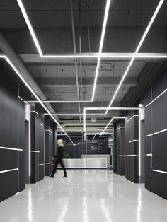 a person walking down a long hallway with lights on either side of the wall and ceiling