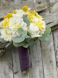 a bridal bouquet with yellow and white flowers on a piece of wooden planks