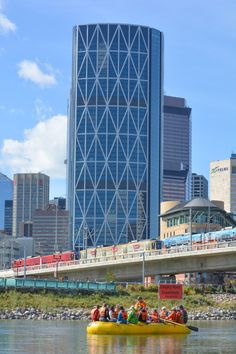 a group of people riding on top of a yellow raft down a river next to tall buildings