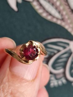 a close up of a person's hand holding a ring with a red stone