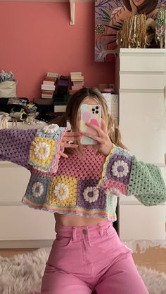 a woman taking a selfie while wearing pink pants and a crocheted sweater