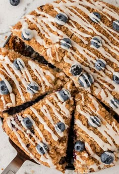 a blueberry crumb cake with white icing on a marble counter top, cut into slices