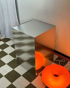 an orange donut sitting on top of a checkered floor next to a metal box