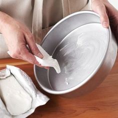 a person in an apron using a spatula to mix batter into a cake pan