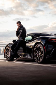 a man sitting on top of a black sports car