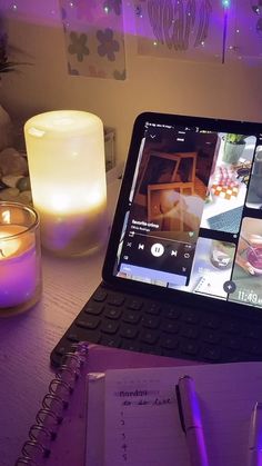 an open laptop computer sitting on top of a wooden desk next to a candle and a book