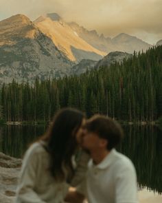 a couple kissing in front of a mountain lake