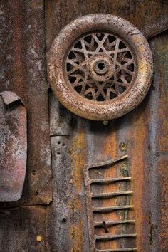 an old rusted metal door with a rusty wheel and ladder hanging on it's side