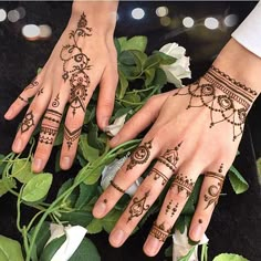 two hands with henna tattoos on them and flowers in the foreground, one is holding onto another hand