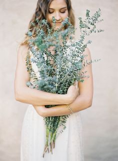 a woman wearing a white dress holding a bouquet of flowers and greenery in her hands