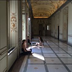 two people are sitting on the floor in an ornate hallway with white walls and marble floors