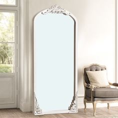 a large white mirror sitting in the corner of a room next to a chair and window