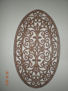 an oval metal wall hanging on the side of a white wall with scrolly filigrees