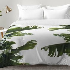 a bed with white sheets and green palm leaves on the comforter, next to a lamp