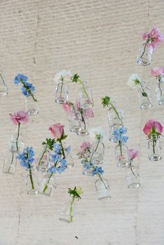 several glass vases filled with flowers hanging from the ceiling in front of a wall